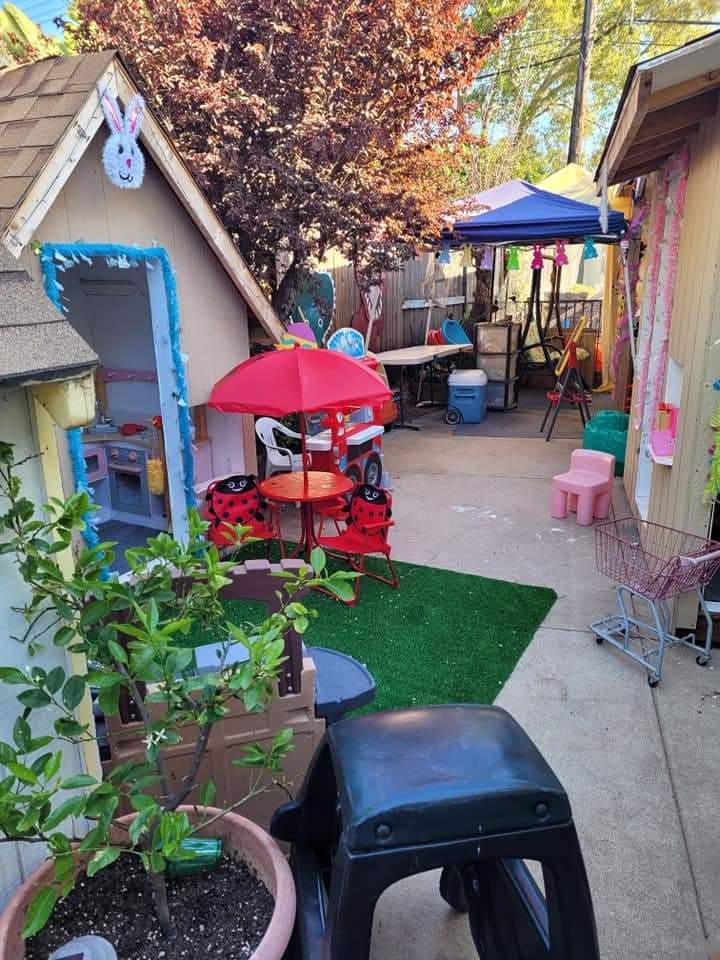 Backyard play area with a small playhouse, red umbrella, and various toys