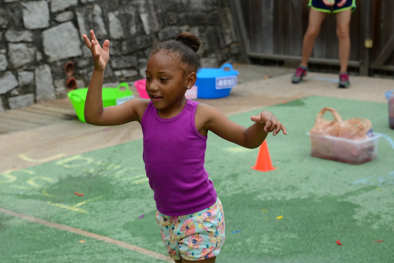 Child with arms raised, standing on green ground