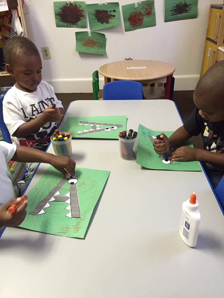 Children at a table doing crafts with green paper and googly eyes