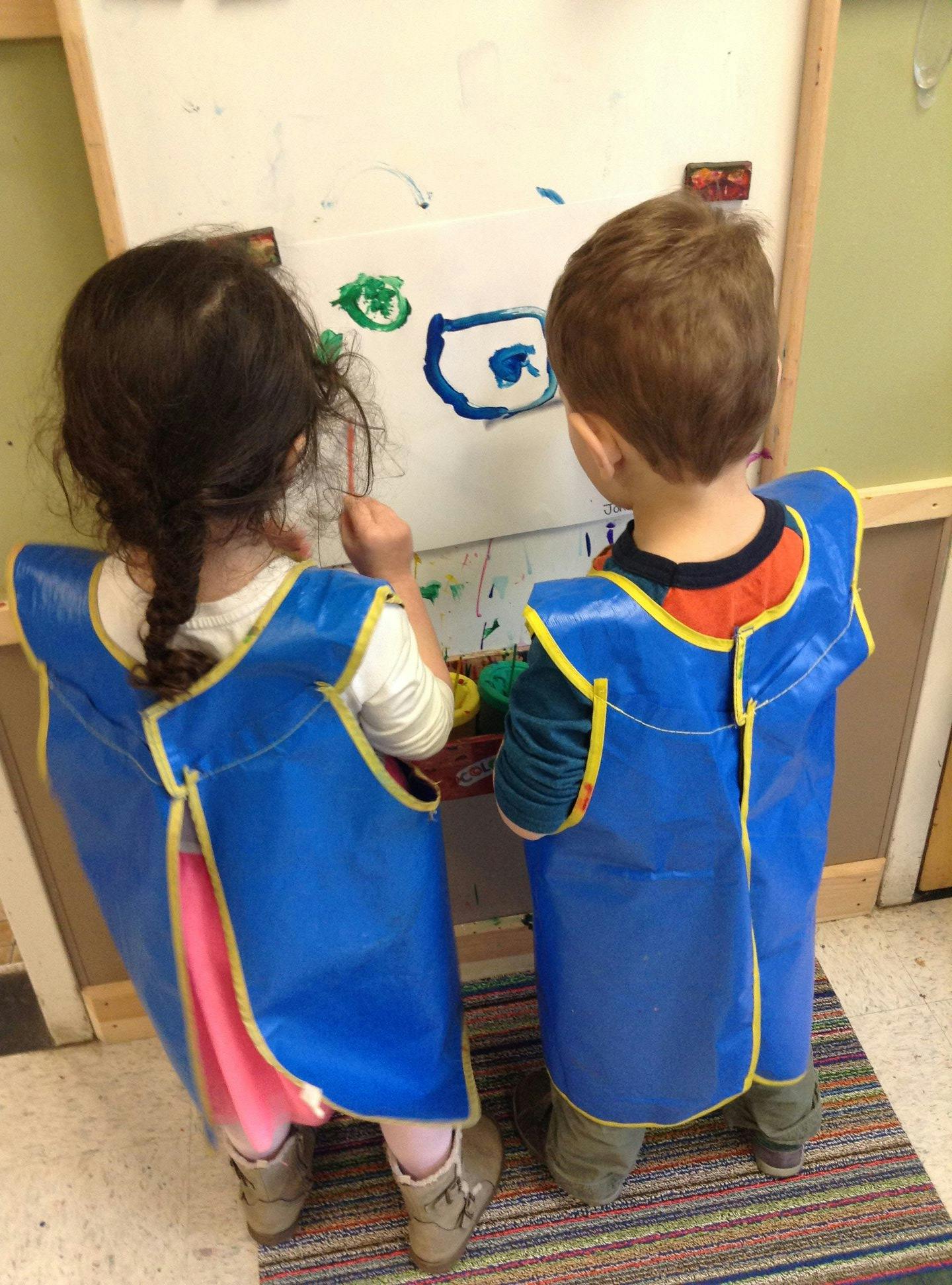 Two children in smocks painting at an easel