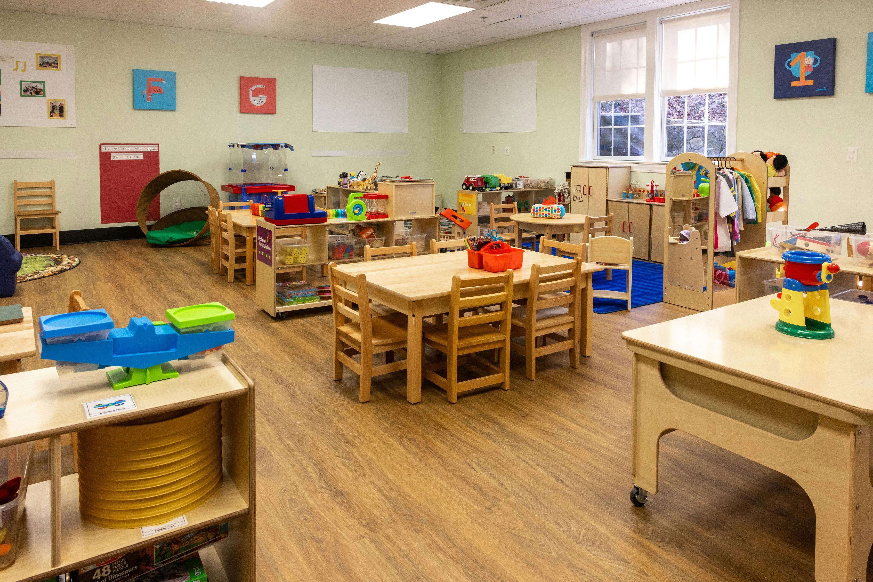 An empty early childhood classroom with multiple wooden tables and chairs