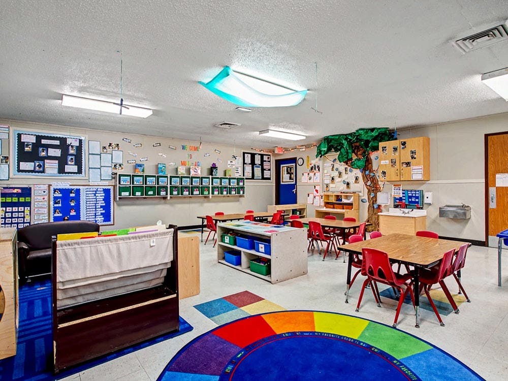 Empty classroom with small tables and chairs, and a colorful rug