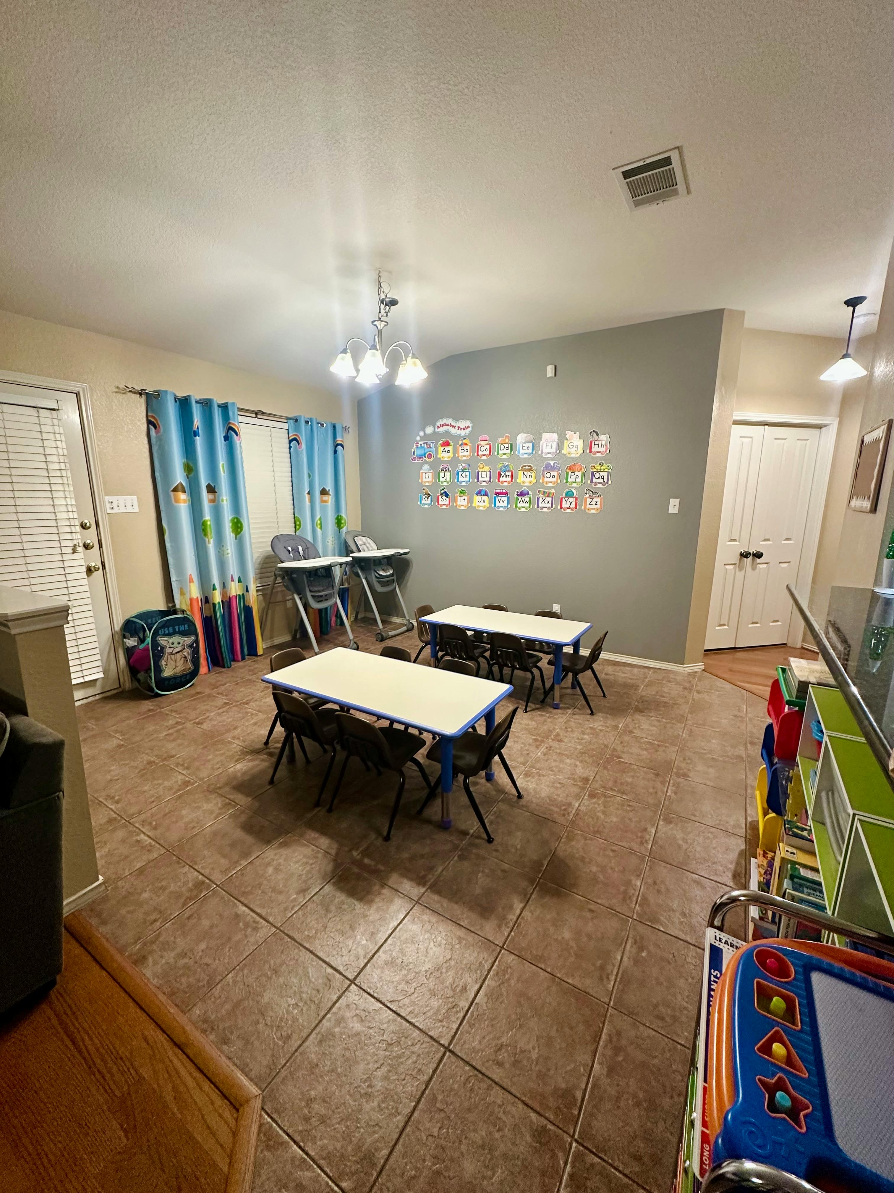 Classroom with small tables and chairs, high chairs, and wall decorations