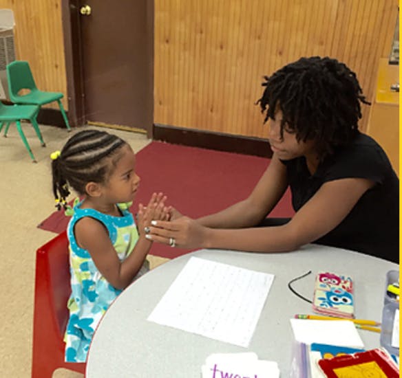 Adult and child sitting at a table, hands clasped