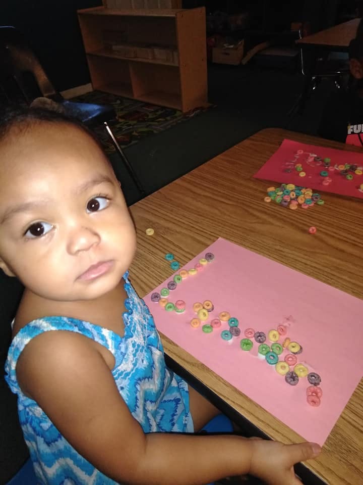 Child sitting at a table with colorful cereal pieces on pink paper