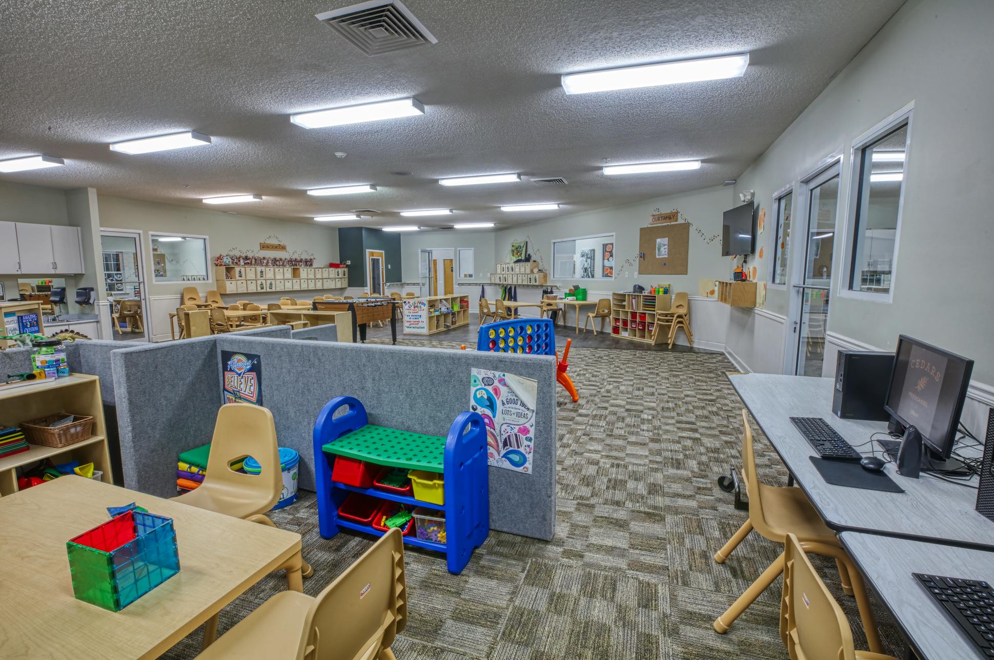 An empty childcare classroom with small tables, chairs, and play areas
