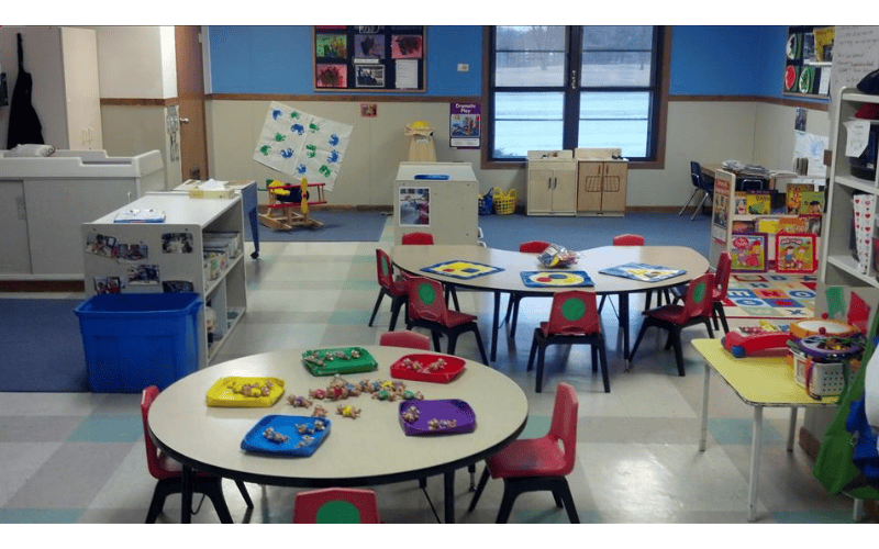 Empty classroom with small tables and chairs, toys on tables, and storage units
