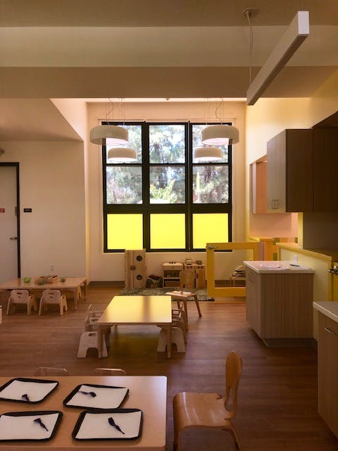 Classroom with small tables and chairs, large window with yellow panels