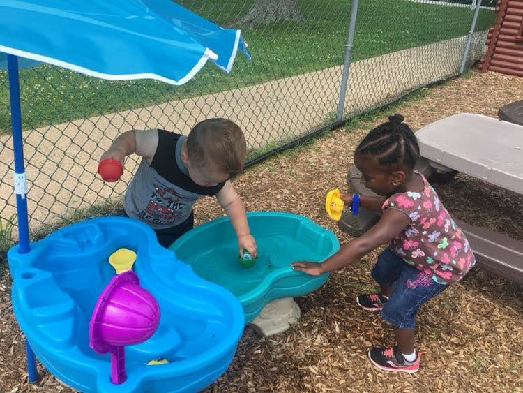Two children playing with a water table outdoors