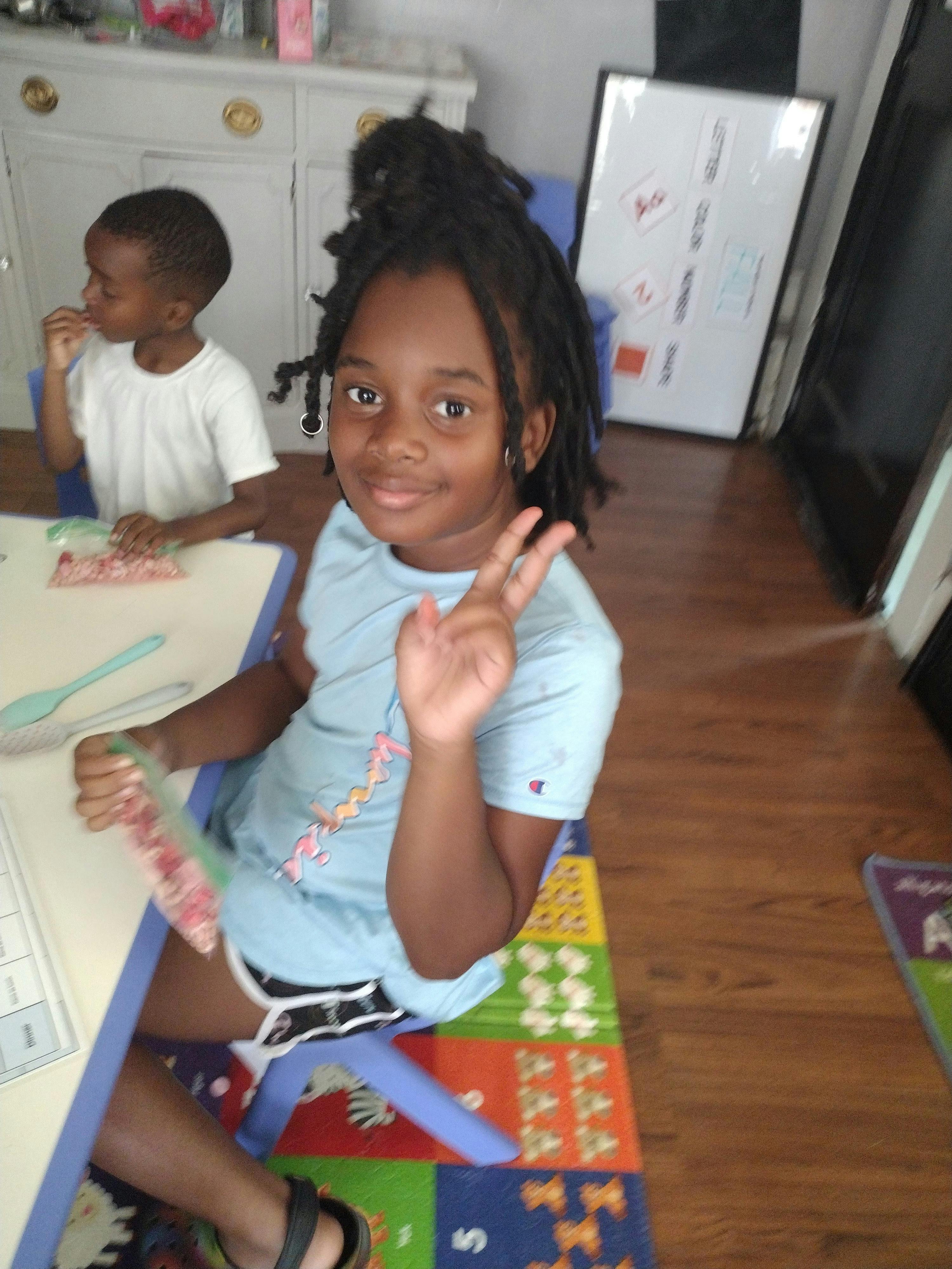 Child making a peace sign at a table with another child in the background