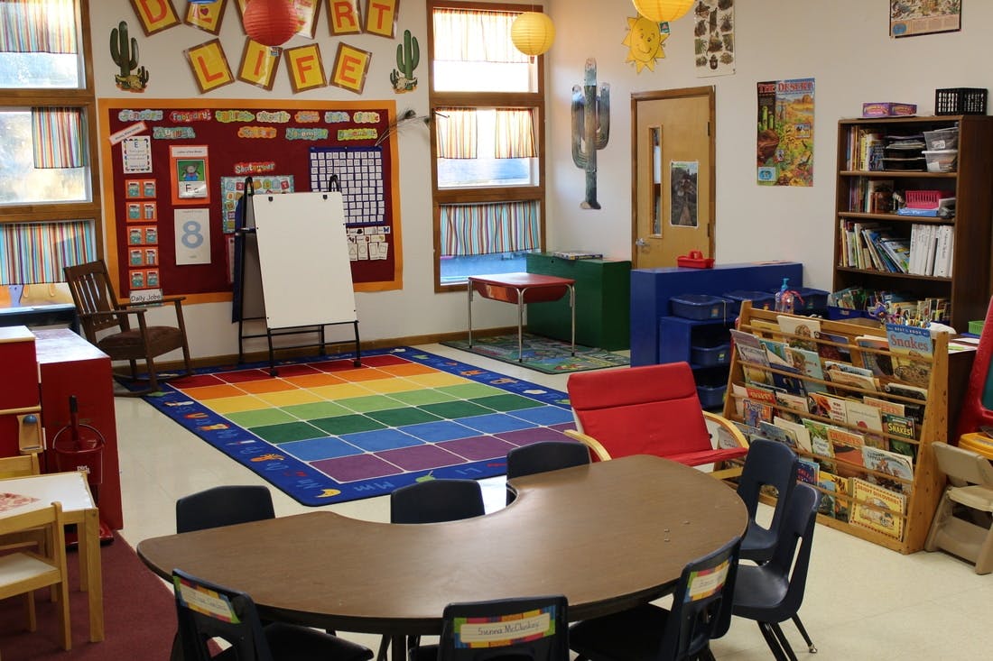 Classroom with a rainbow rug, tables, chairs, and a whiteboard
