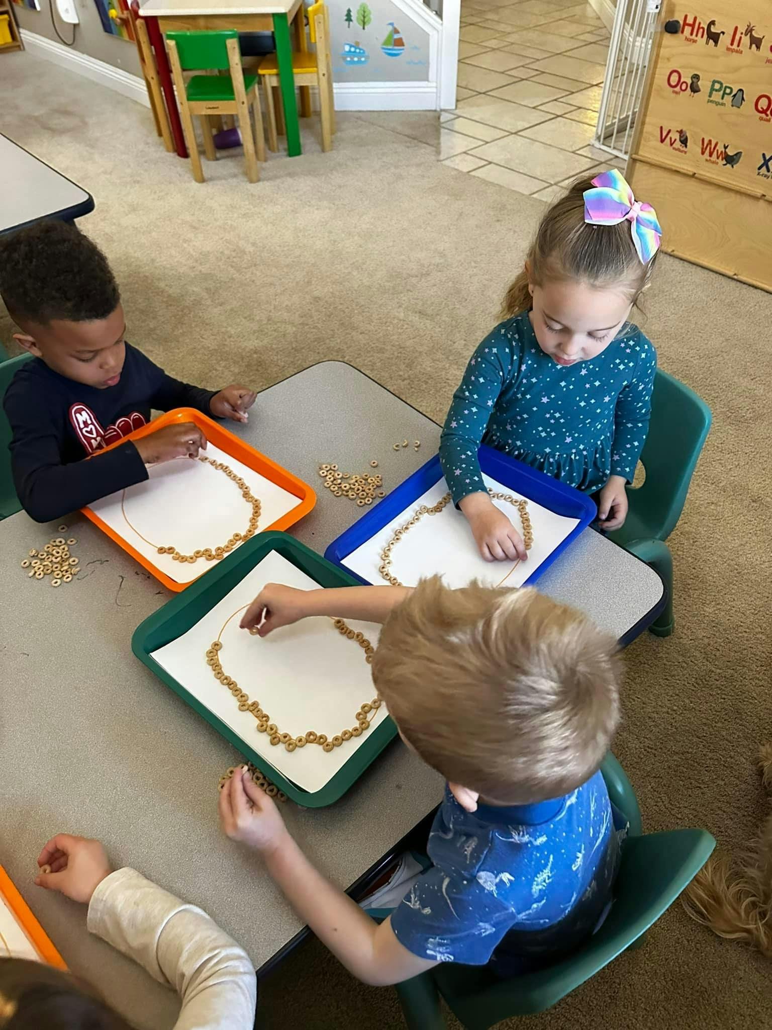 Three children at a table making designs with cereal pieces