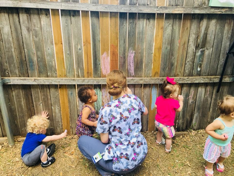 Person and three children drawing with chalk on a wooden fence