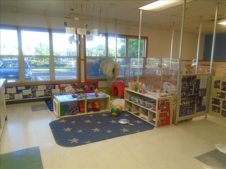daycare classroom with tables of toys, cribs in background, and windows overlooking outside