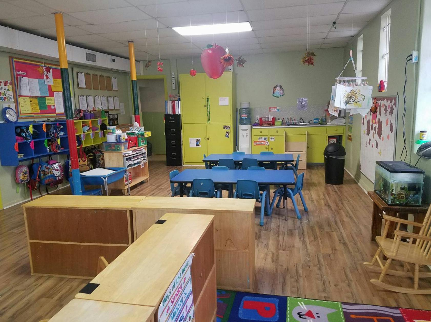 Classroom with blue tables and chairs, wooden storage units, and a fish tank