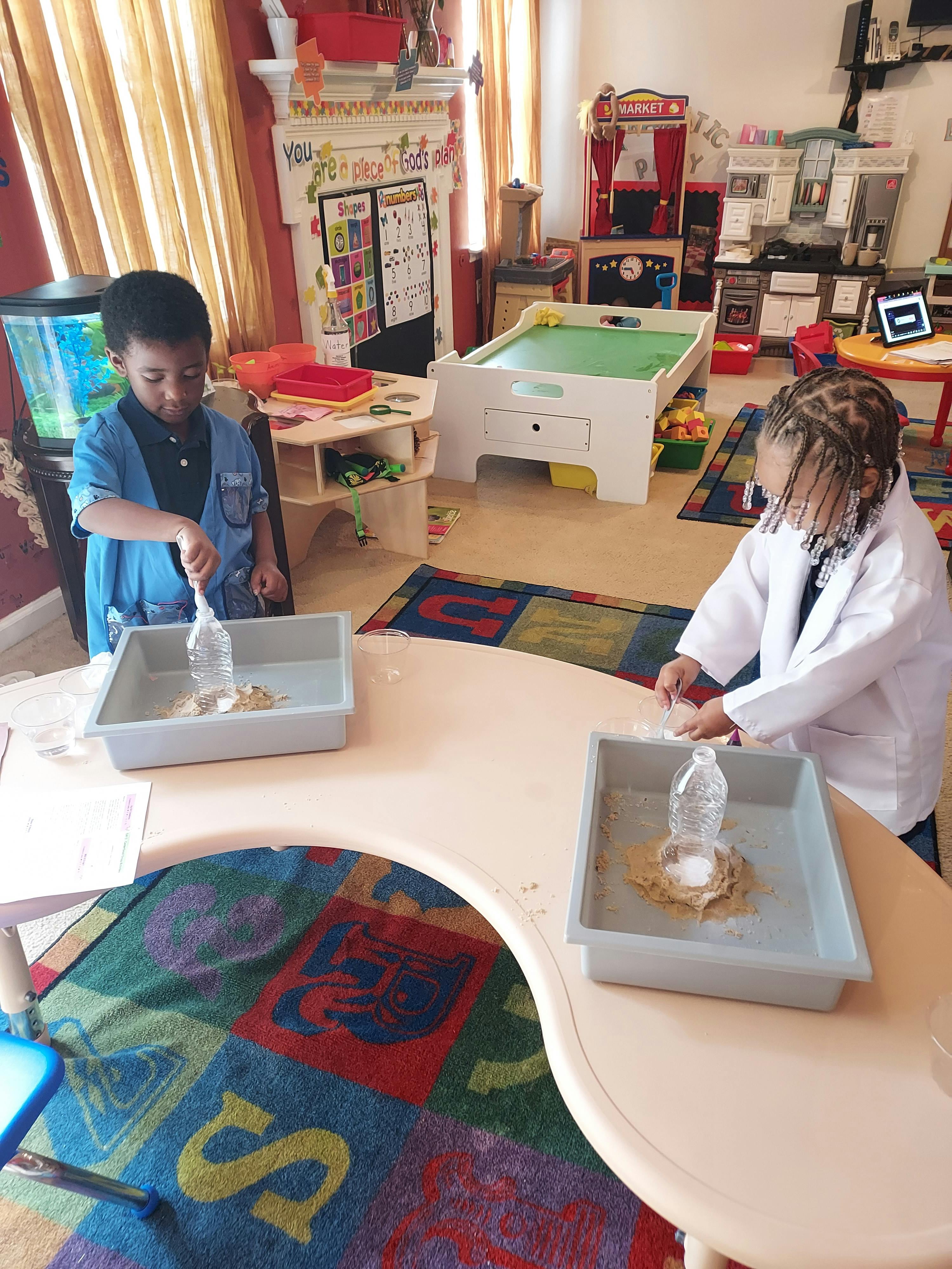 Two children playing with water and sand in trays on a table in a classroom
