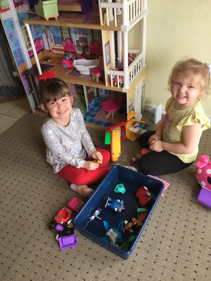 Two children playing with toys on the floor next to a dollhouse