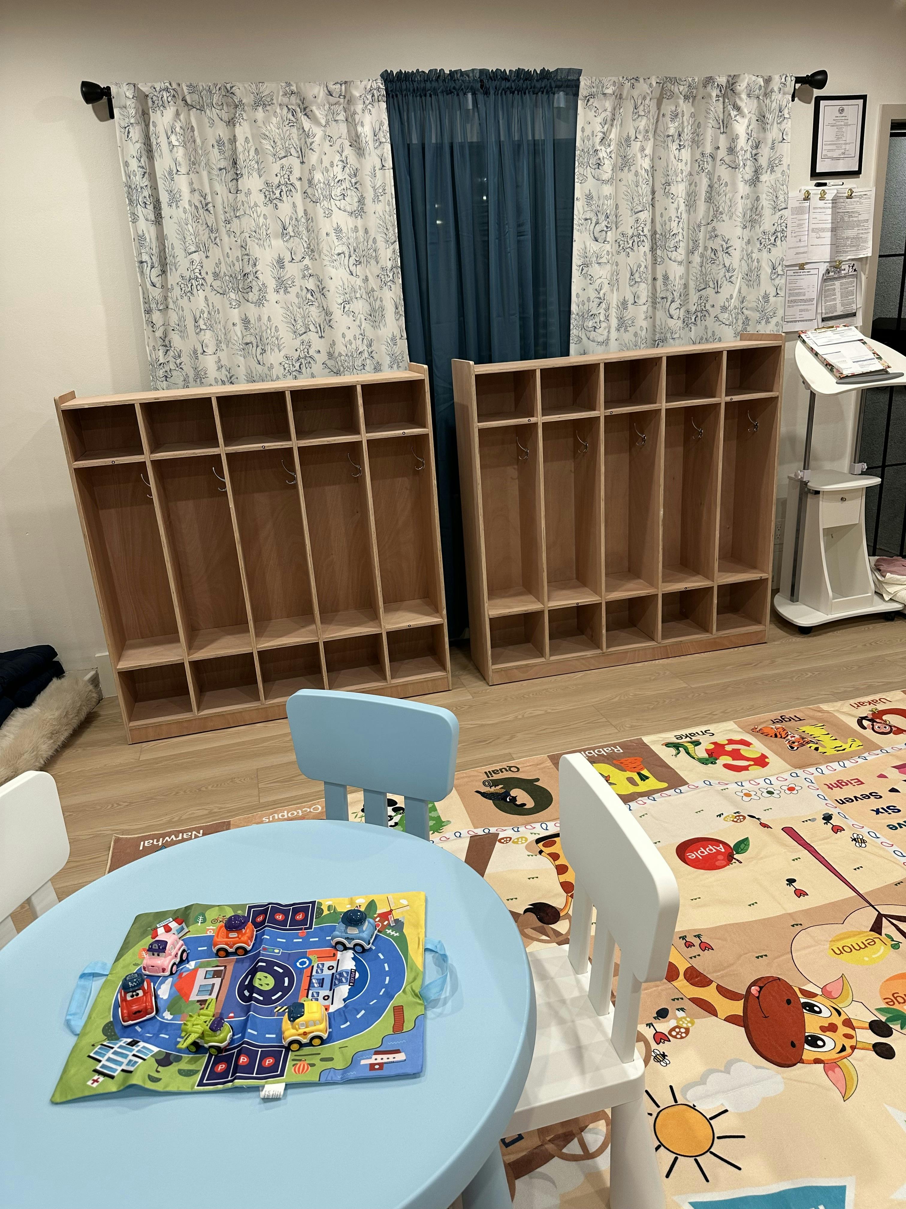 Children's classroom with small table, chairs, playmat, and cubbies