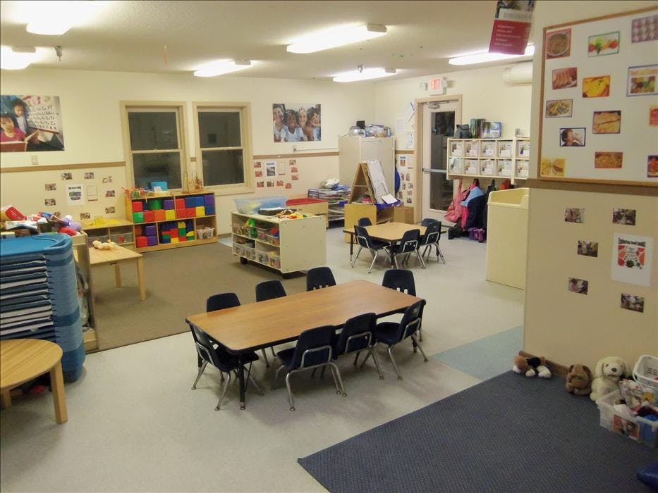 Classroom with small tables, chairs, and shelves with toys and learning materials