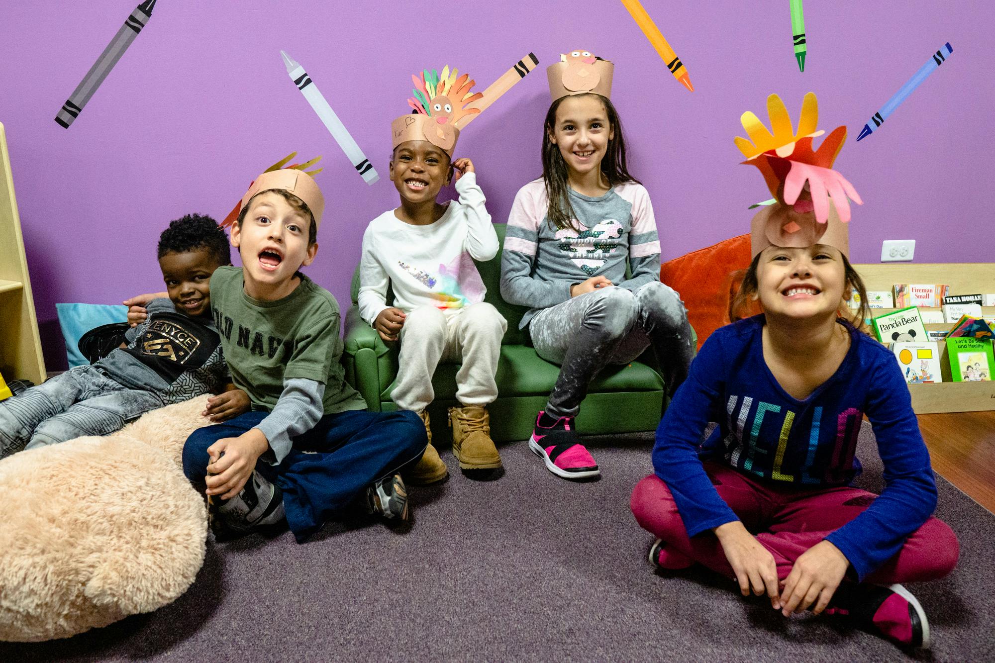 Children wearing paper crowns, some sitting on a couch, some on the floor