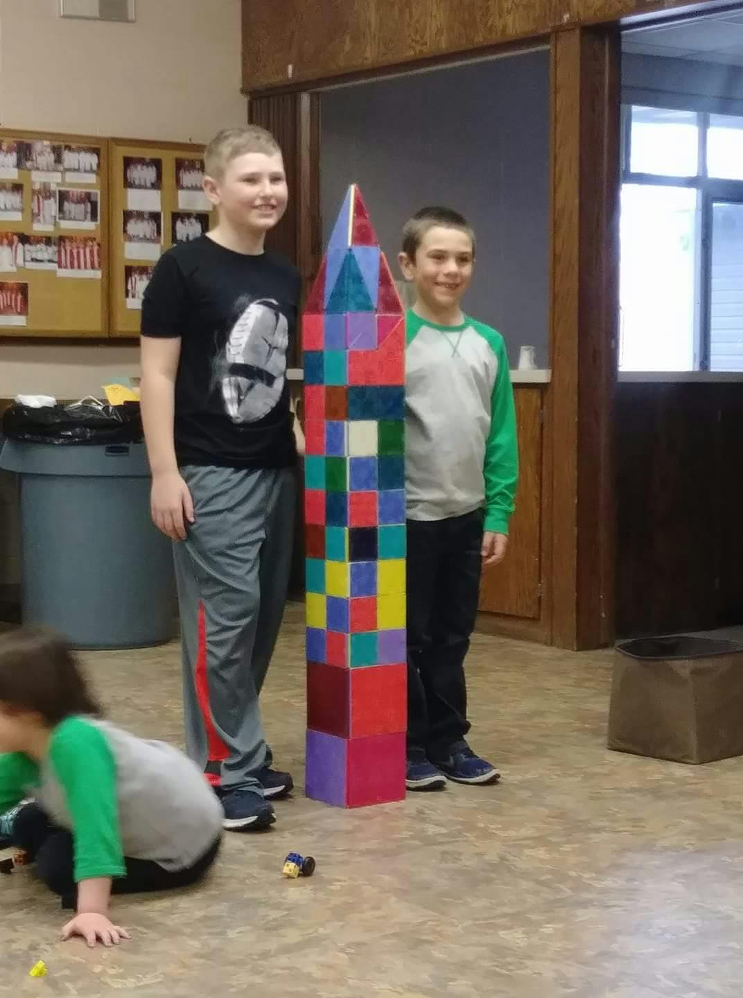 Two children standing next to a tall, colorful block structure