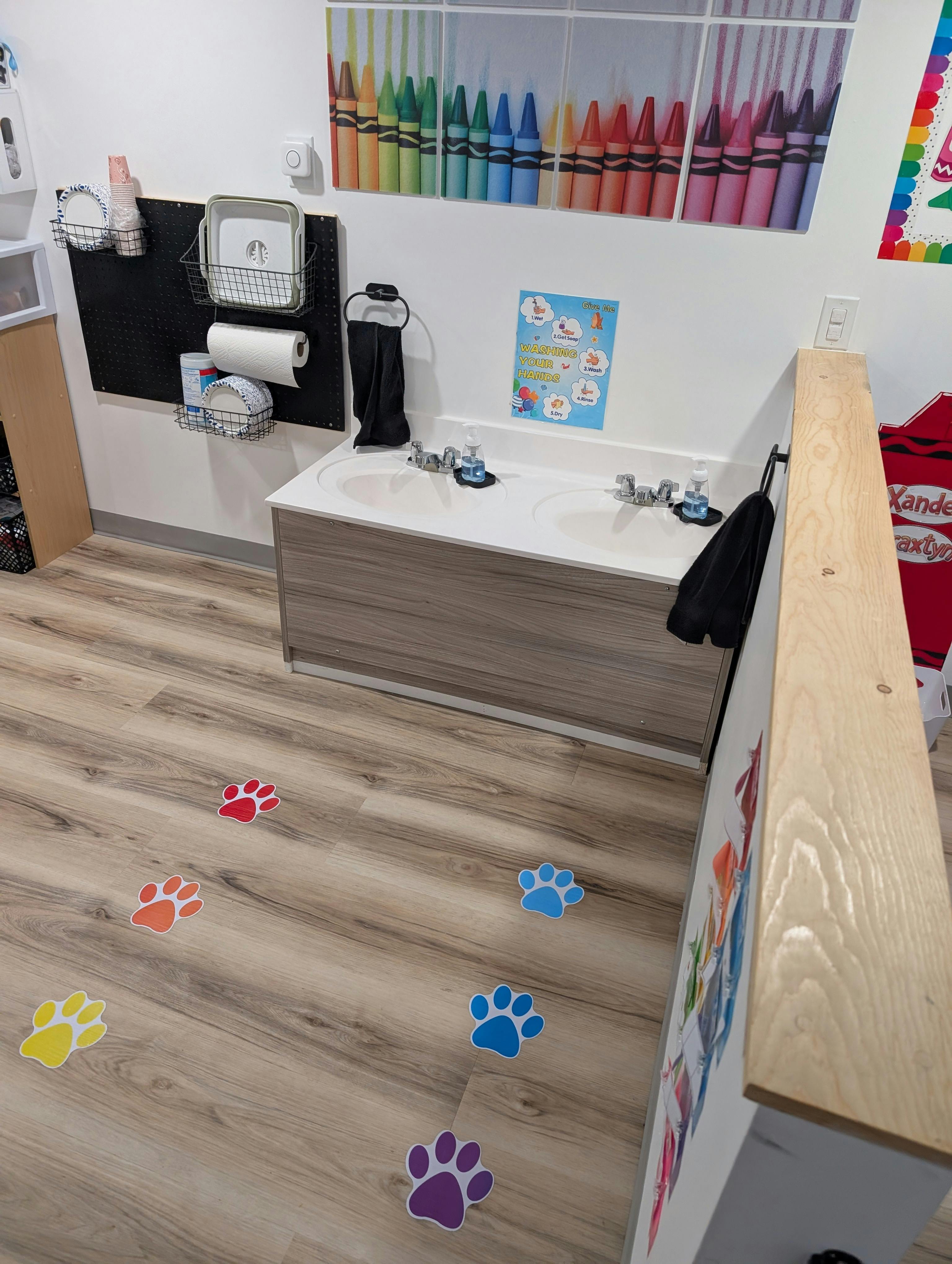 Classroom with two sinks, paper towel dispenser, and colorful paw print decals on the floor