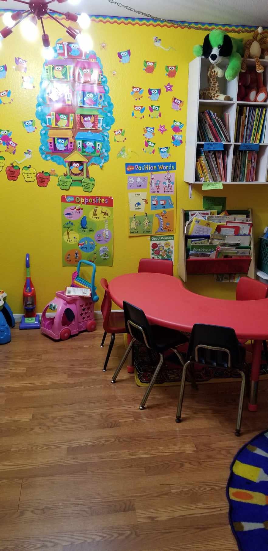 Classroom with a red kidney-shaped table and chairs, toys, and educational posters
