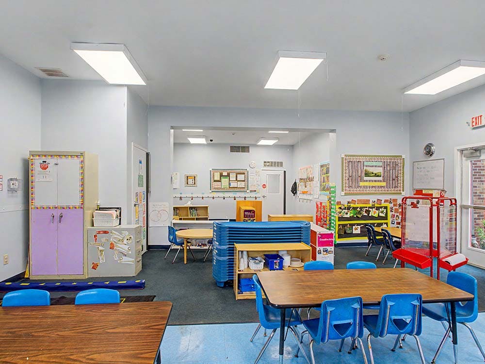 Classroom with small tables and blue chairs, educational displays on walls