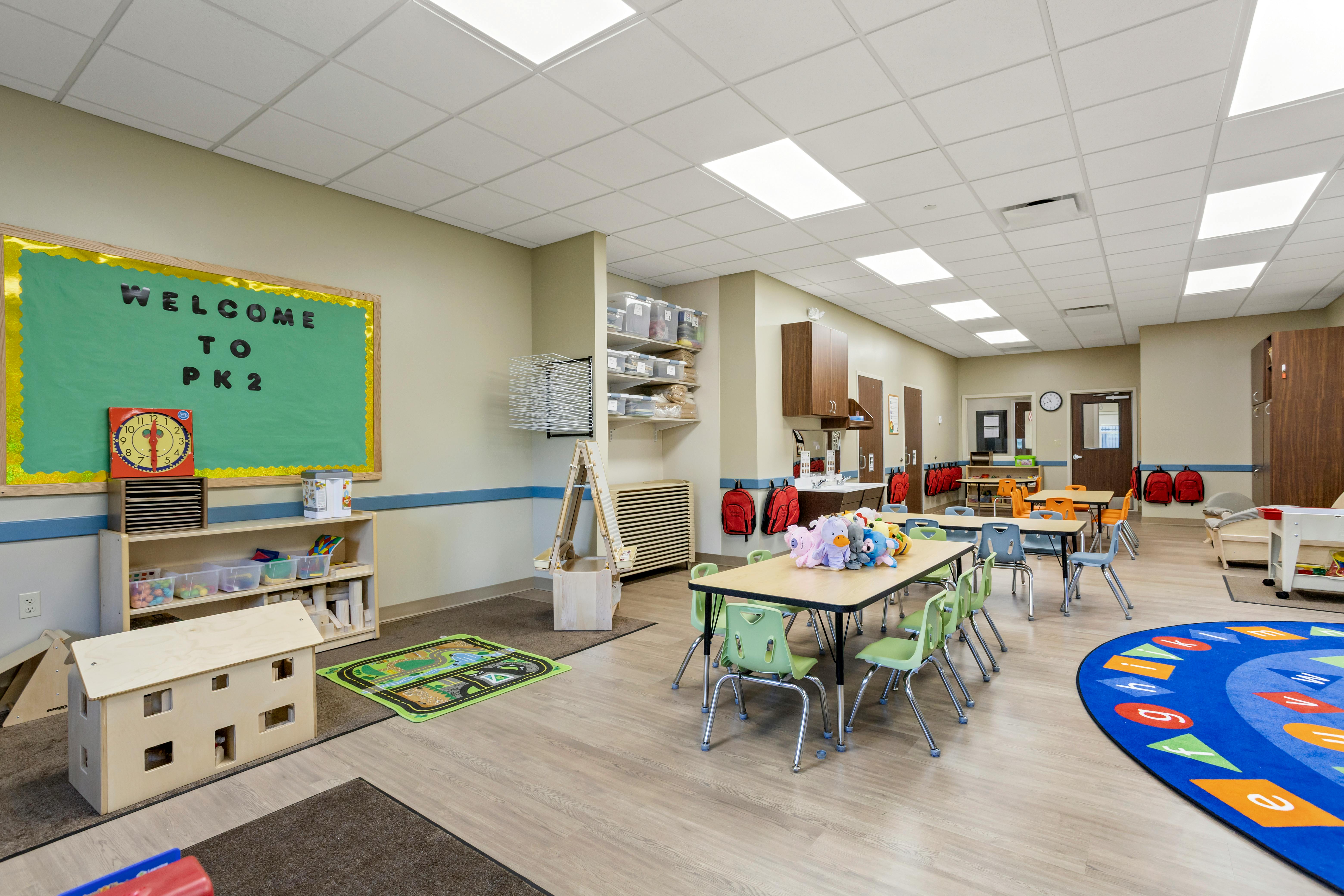 Classroom with small tables, chairs, and a \"Welcome to PK2\" bulletin board