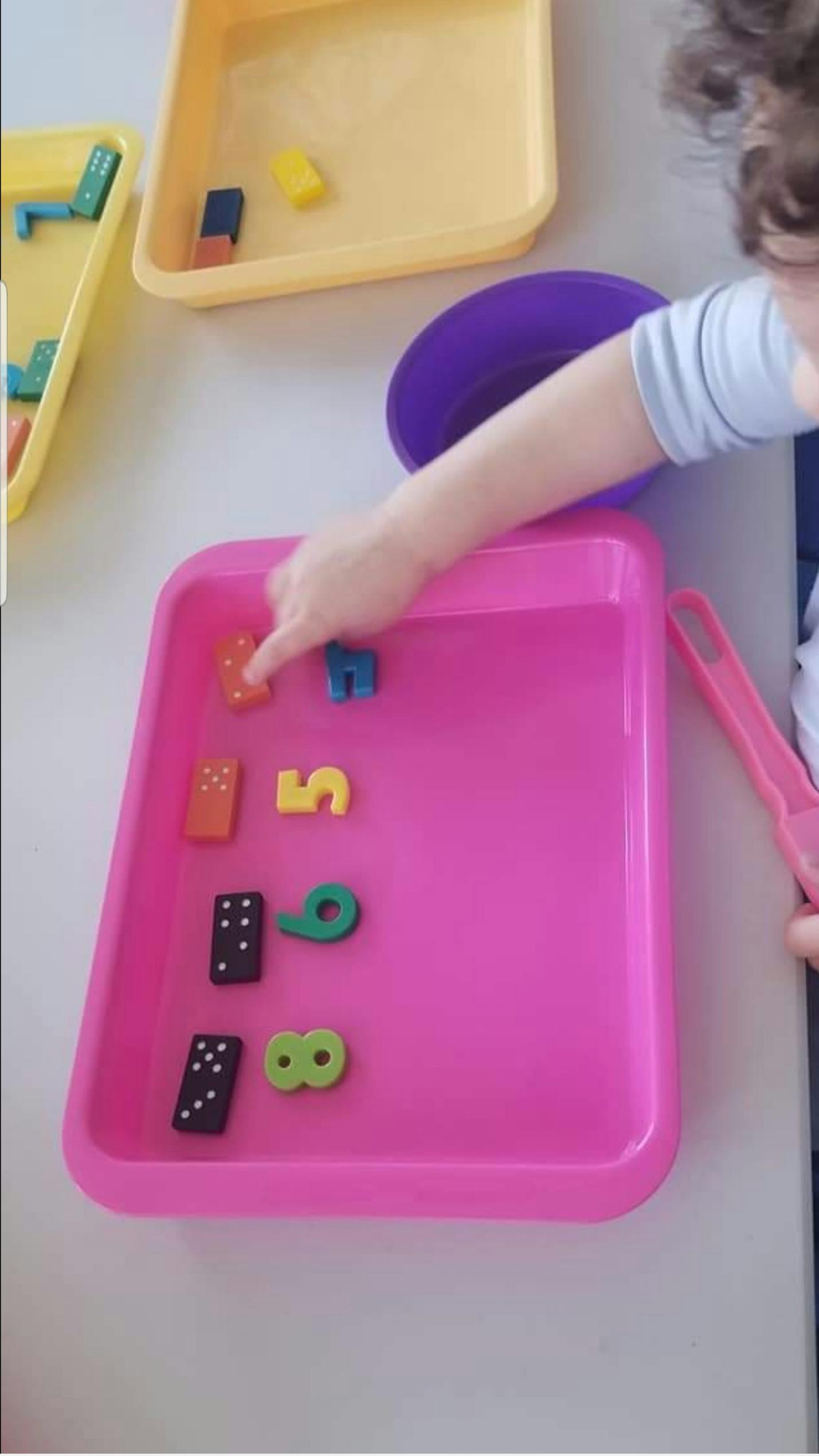 Child's hand touching colorful number and domino pieces in a pink tray