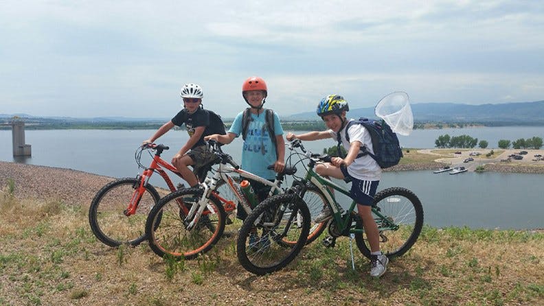 Three children with bicycles on a hill overlooking water