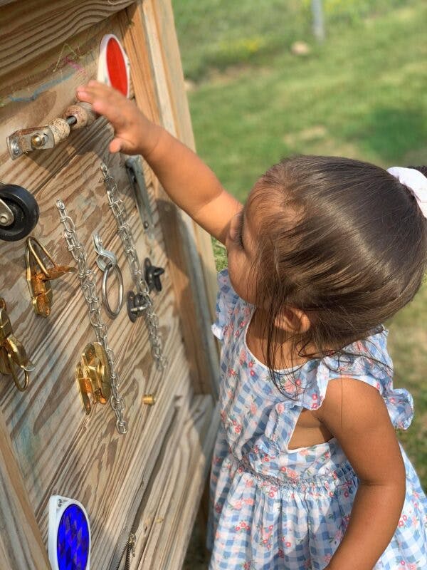Child reaching for a red button on a wooden activity board