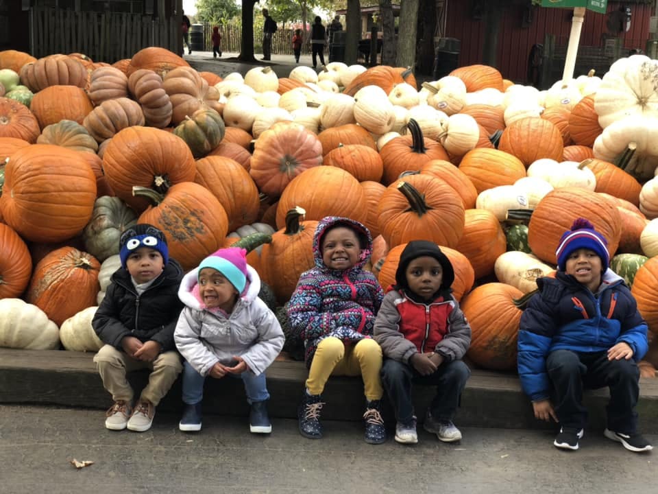 Four children sitting in front of a large pile of pumpkins