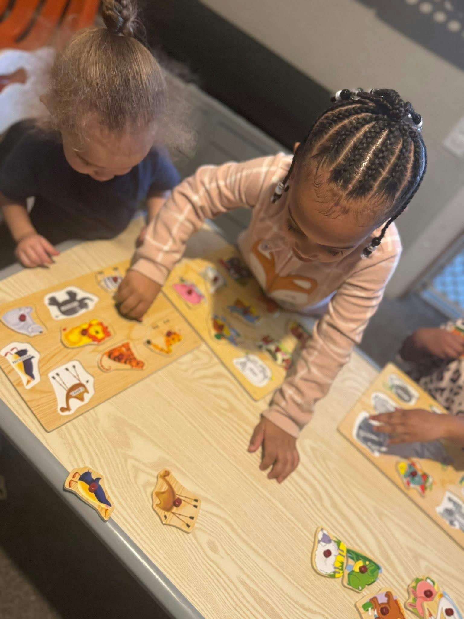 Three children solving animal shaped wooden puzzles at a table
