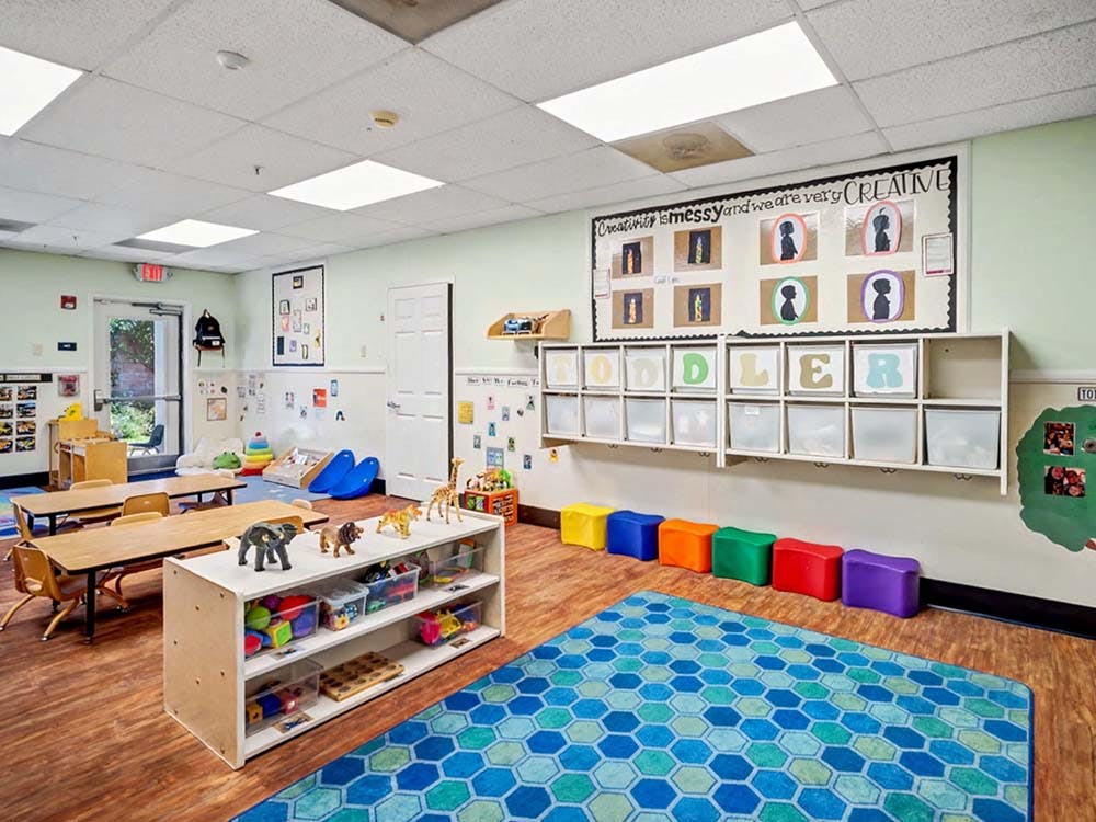 A colorful toddler classroom with toys, small tables, and a storage unit