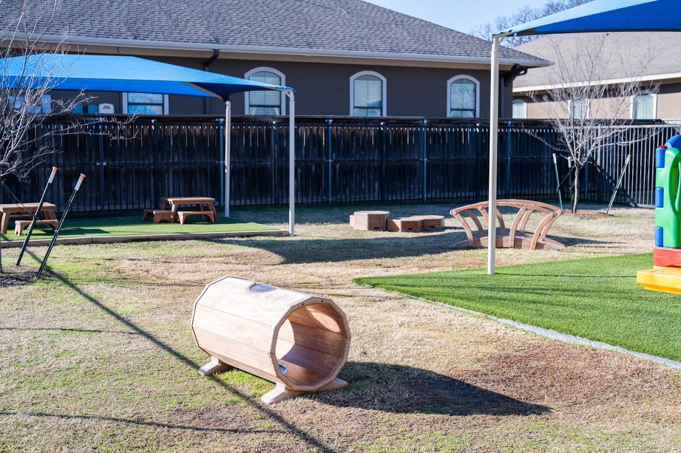 Wooden play tunnel and equipment in a fenced outdoor playground