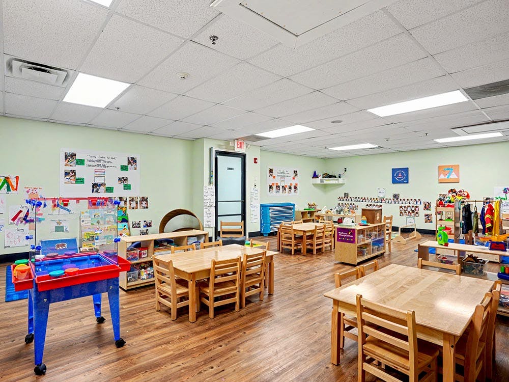 Empty classroom with small wooden tables and chairs, toys, and art on walls