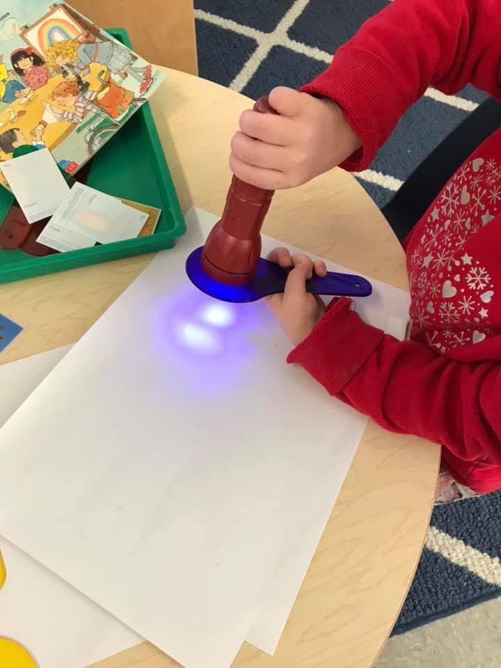 Child holding a flashlight with a purple light shining on white paper