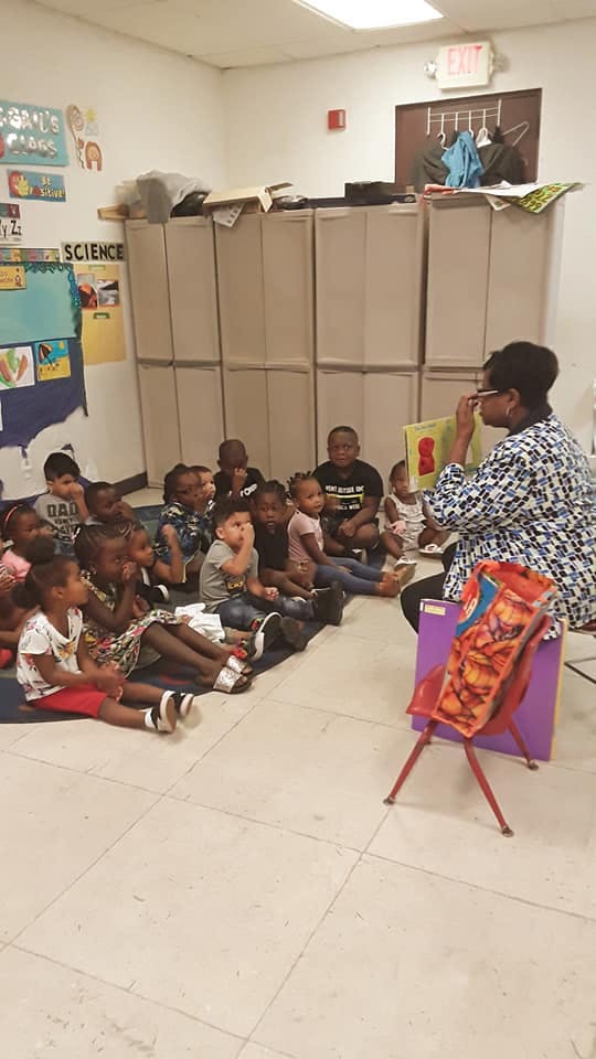 Person reading a book to a group of children in a classroom