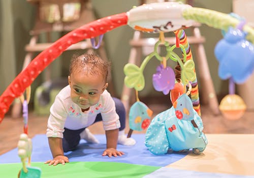 Child crawling on a playmat with toys