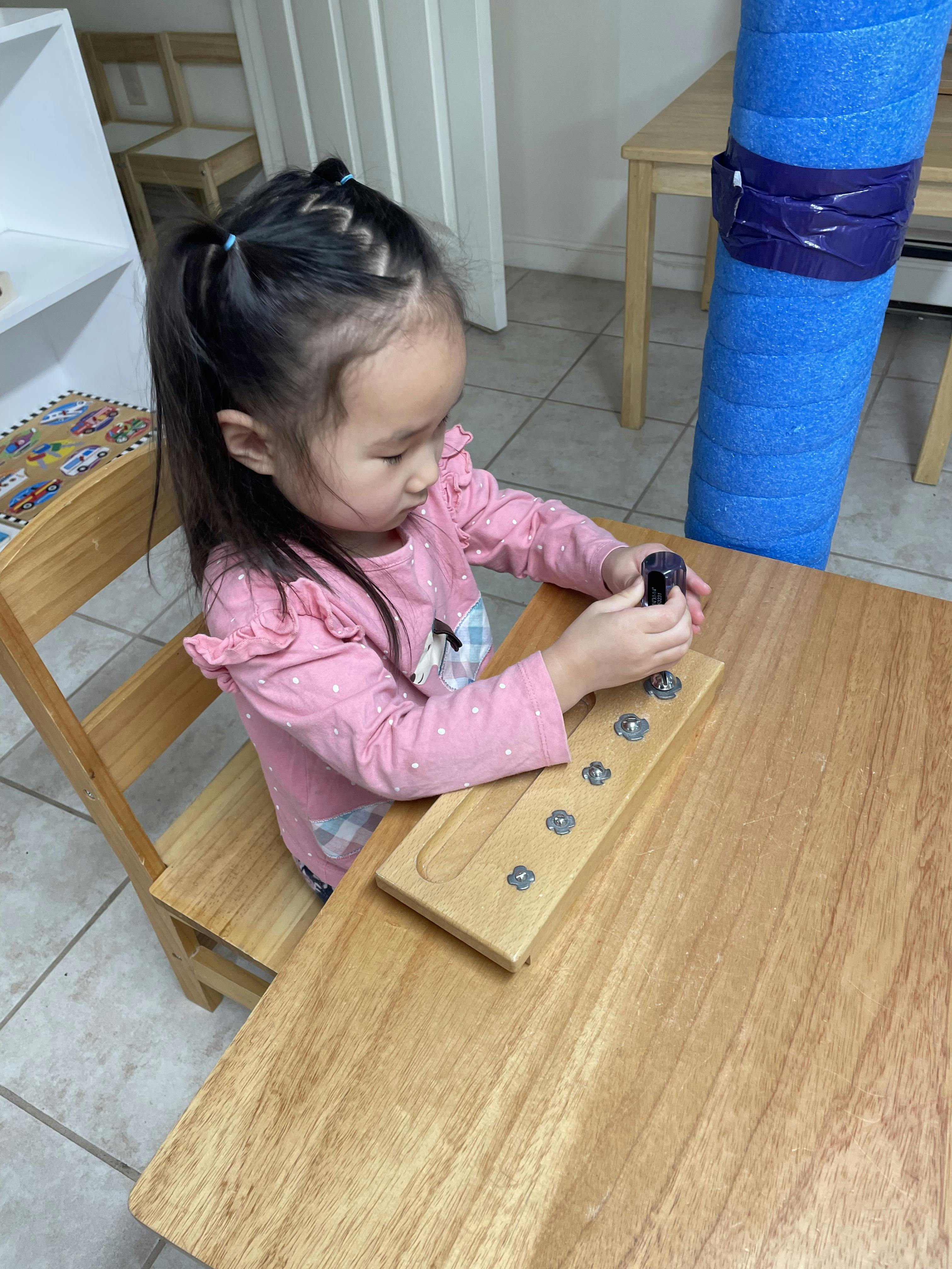 Child using a tool on a wooden board with bolts