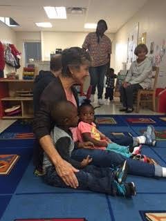 Adult sitting on floor with two children, other adults and child in background