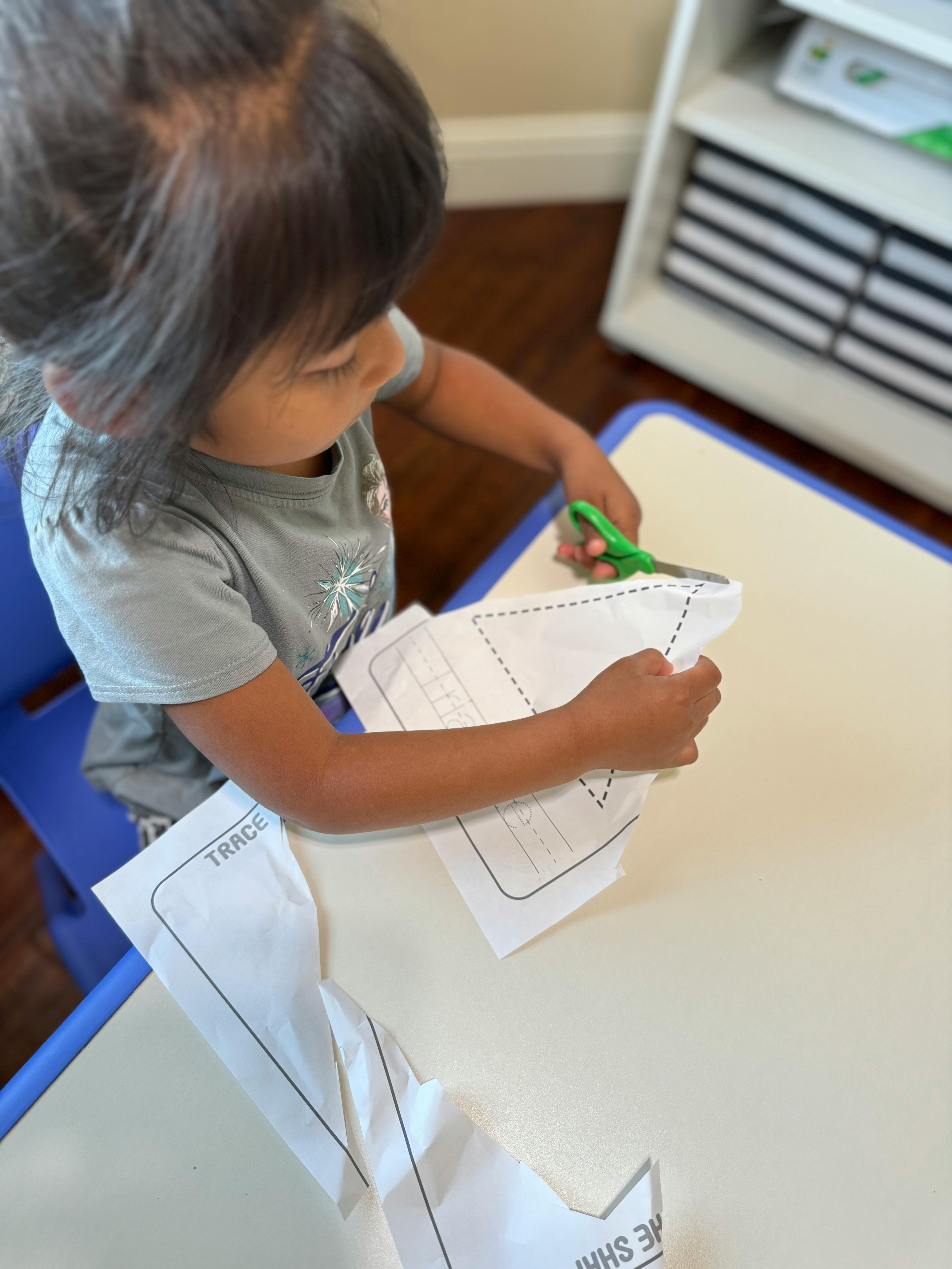 Child cutting paper with scissors at a table