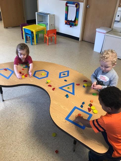 Three children playing with colorful shapes on a classroom table