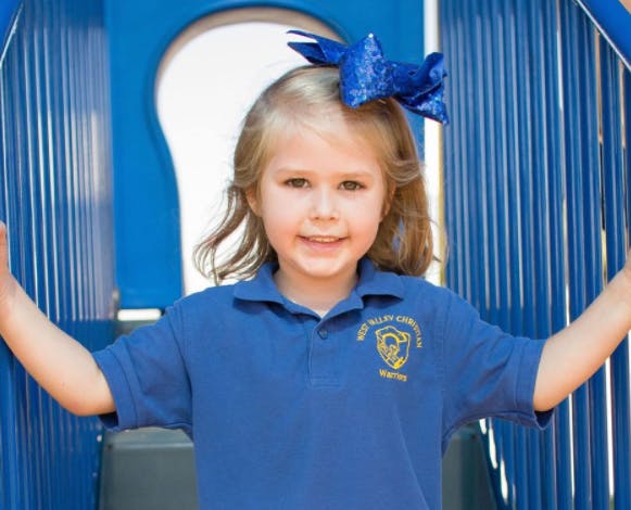 Child in blue shirt with a bow in hair standing on a playground