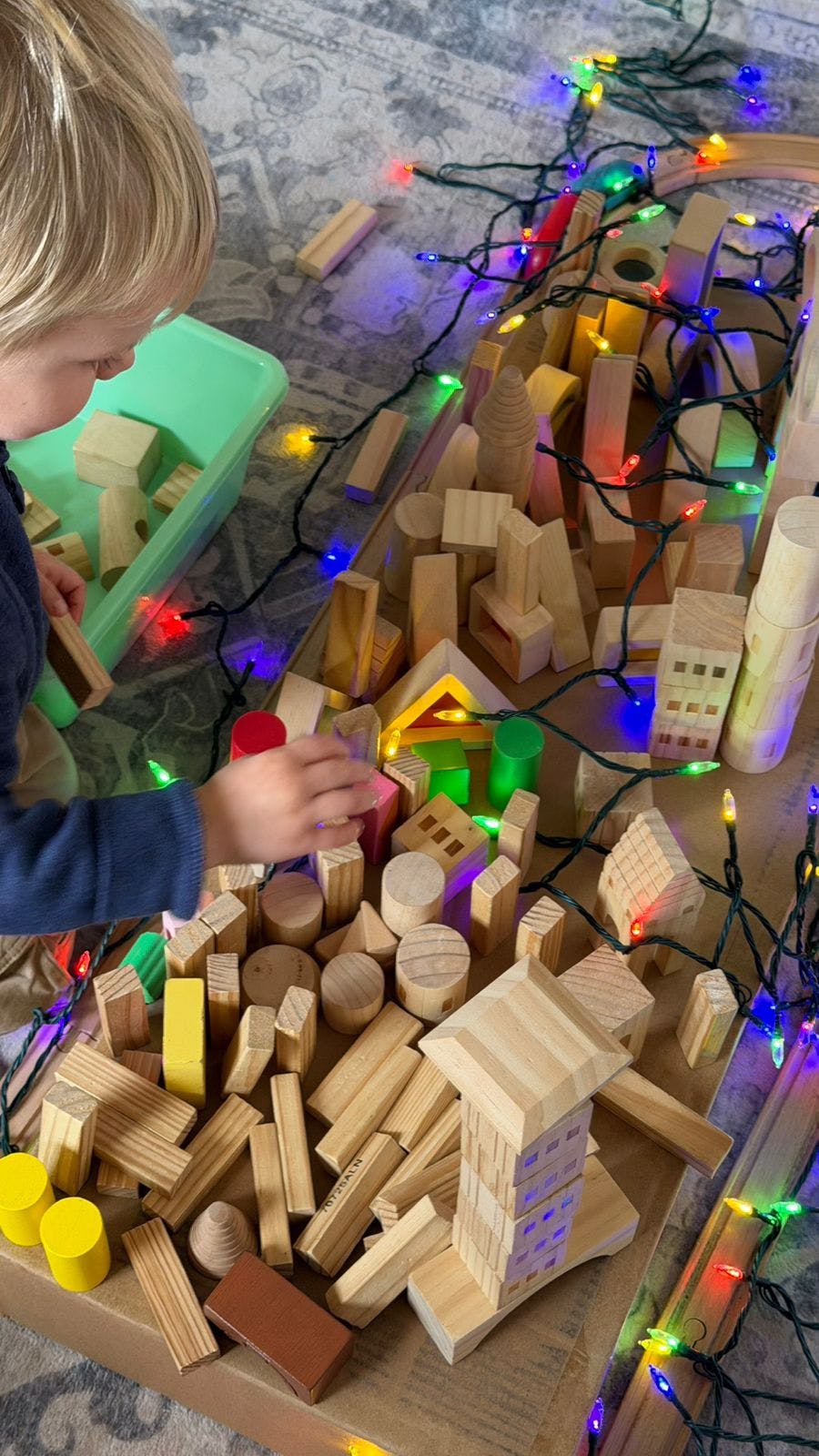 Child playing with wooden blocks and string lights