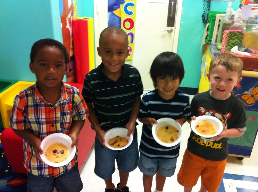 Four children holding bowls of food in a classroom