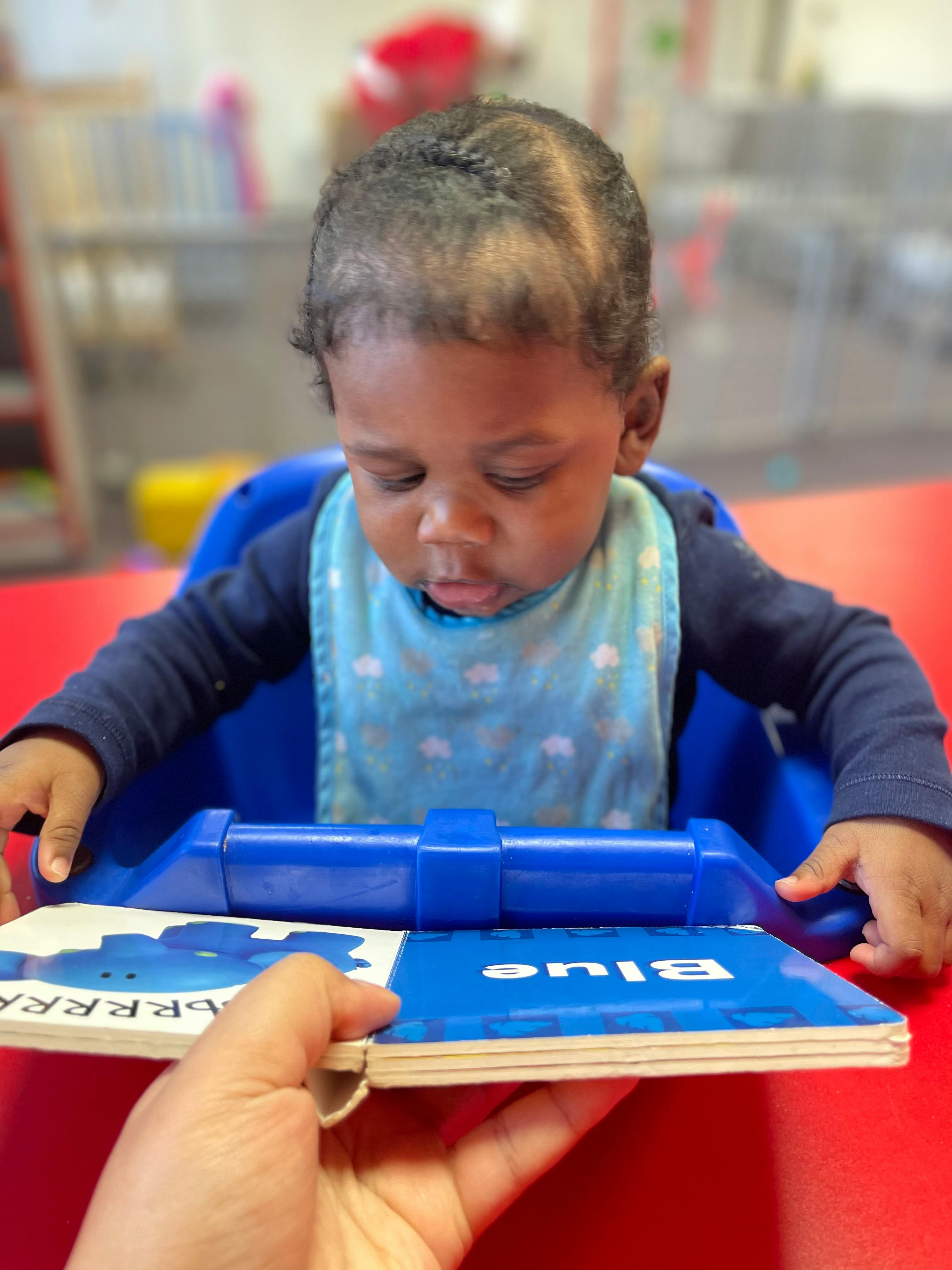 Child in a high chair looking at a book held by an adult