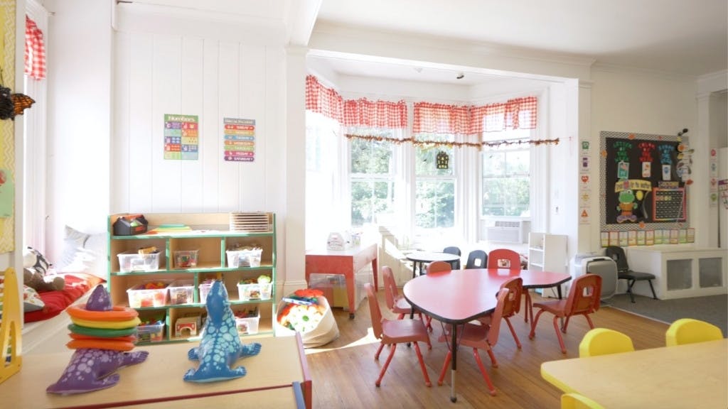 Classroom with small tables and chairs, shelves with toys