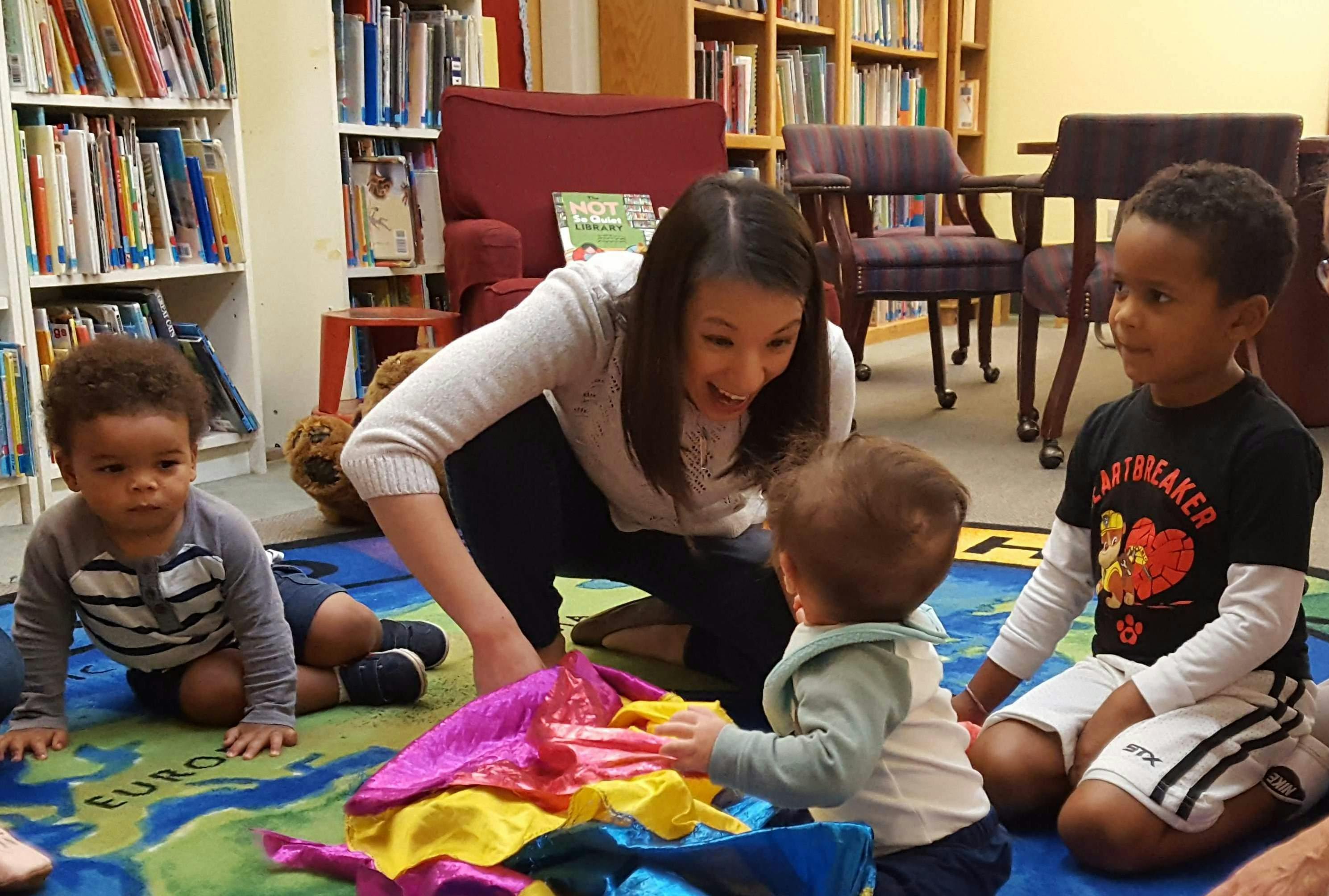 Person interacting with three children on a rug in a library